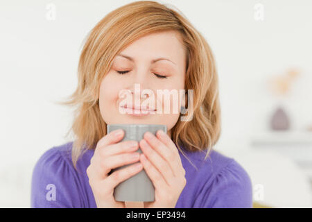 Prety i capelli rossi donna holding e annusare una tazza di caffè mentre è seduto su un divano Foto Stock