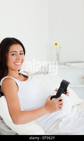 Attraente donna incinta mettendo le cuffie sul suo ventre mentre giaceva su un letto Foto Stock
