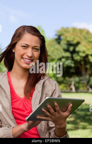 Donna sorridente e guardando avanti mentre lei usa una compressa in un parco Foto Stock
