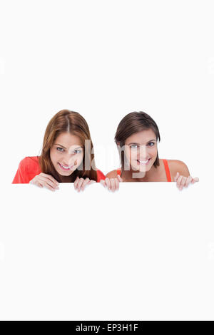 Le ragazze adolescenti a sorridere mentre si tiene un poster in bianco e nascondersi dietro di essa Foto Stock