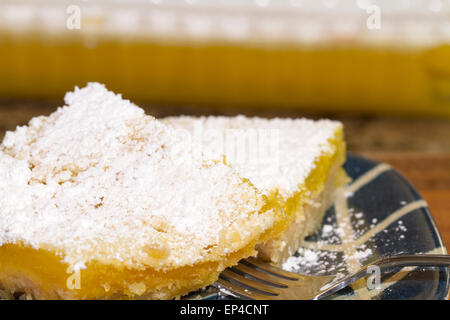 Lemon Bar che serve appena sostenuto e coperto di zucchero a velo. Servita su un blu e piastra bianca Foto Stock