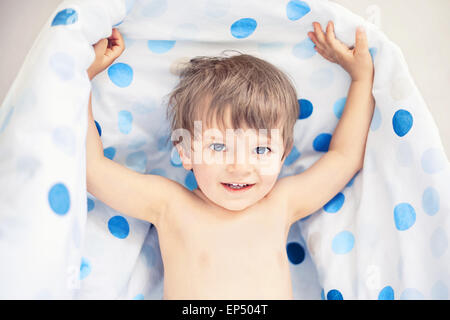 Sorridente ragazzino che tiene coperta dopo aver dormito Foto Stock