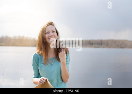 Sorridente e felice ragazza con il cappello in mano sul lago Foto Stock