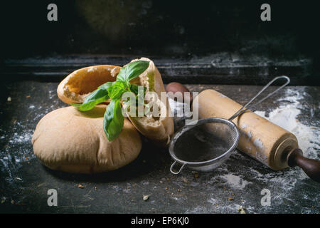 Due fatti in casa e intere fette di pane pita farcita con basilico fresco, servita con farina, vintage mattarello e stainer oltre il buio Foto Stock