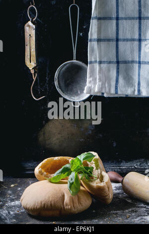 Due fatti in casa e intere fette di pane pita farcita con basilico fresco, servita con farina, vintage mattarello e stainer oltre il buio Foto Stock