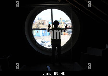 10 anno vecchio ragazzo inglese guardando fuori della finestra del faro in Boa Trinity Wharf faro. Foto Stock