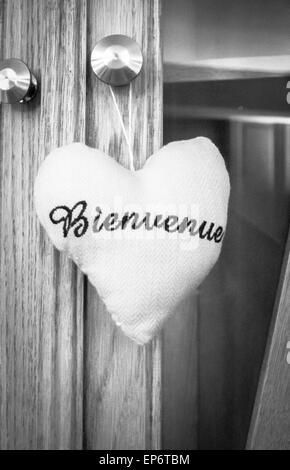 Un materiale di ripiena di cuore con la parola bienvenue (francese per i benvenuti) ricamati su di esso, in bianco e nero Foto Stock