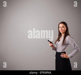Giovane donna in piedi e in possesso di un telefono cellulare con spazio di copia Foto Stock