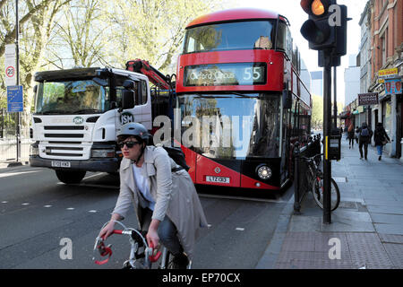 Una femmina di ciclista in sella a una moto da competizione attraverso il semaforo davanti di un 55 red double-decker bus e camion su Old Street London UK KATHY DEWITT Foto Stock