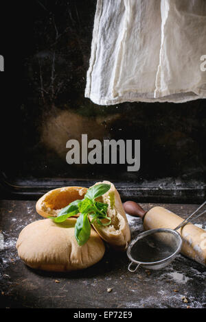 Due fatti in casa e intere fette di pane pita farcita con basilico fresco, servita con farina, vintage mattarello e stainer oltre il buio Foto Stock