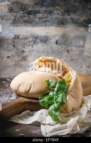 Due fatti in casa e intere fette di pane pita farcita con basilico fresco sul tagliere di legno, servita con la farina sulla tavola scuro Foto Stock