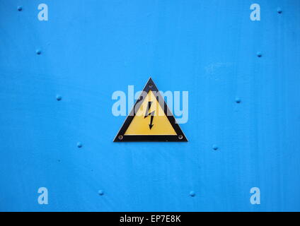 Elettrica gialla triangolo di avvertimento segno su sfondo blu con Rivetter Foto Stock