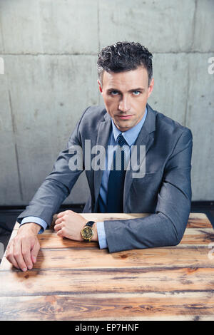 Imprenditore fiducioso seduta al tavolo e guardando la fotocamera Foto Stock