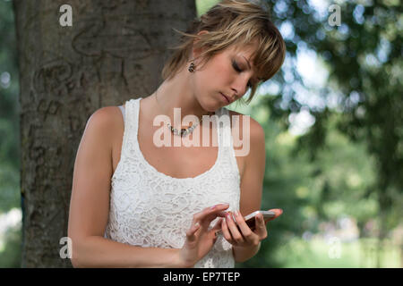 Attraente ragazza bionda all'aperto tramite telefono cellulare, la digitazione e invio di messaggi Foto Stock
