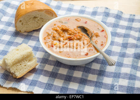 Una ciotola di zuppa di pollo con tortilla su un blu panno selezionata nella finestra di luce con pane francese Foto Stock