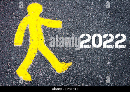 Giallo figura pedonale sulla strada a piedi verso l'anno 2022. Immagine concettuale con un messaggio di testo su sfondo di asfalto. Foto Stock