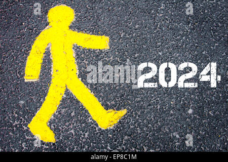 Giallo figura pedonale sulla strada a piedi verso l'anno 2024. Immagine concettuale con un messaggio di testo su sfondo di asfalto. Foto Stock