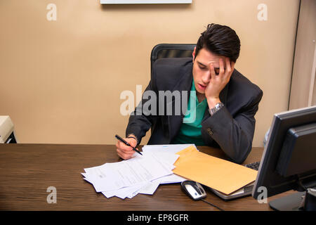 Stanco annoiato giovane imprenditore seduto alla sua scrivania davanti al suo computer sbadigli, con il mento appoggiato sulla sua mano e gli occhi c Foto Stock