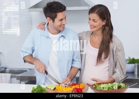 L'uomo tritare verdure accanto al suo partner in stato di gravidanza Foto Stock