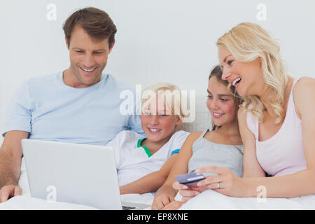 La famiglia tramite computer e una carta di credito a letto Foto Stock