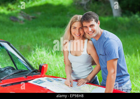 Felice coppia giovane lettura mappa sulla loro cabriolet cofano Foto Stock