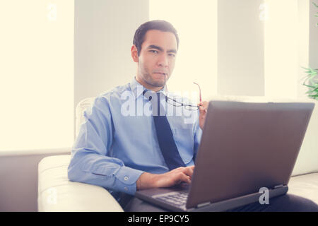 Uomo nervoso mordere i suoi occhiali e utilizzando un computer portatile Foto Stock