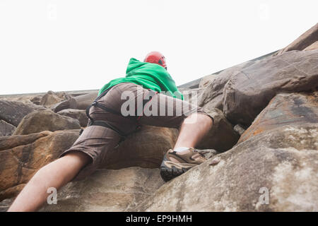 Determinato uomo salire una grande parete di roccia e vedendo la parte superiore Foto Stock