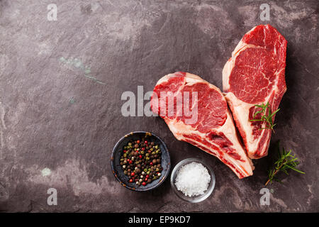 Forma di cuore crudo fresco di carne Ribeye con rosmarino, pepe e sale sulla pietra sullo sfondo di ardesia Foto Stock