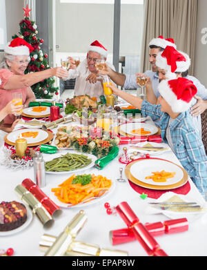 La famiglia in cappelli di Babbo Natale tostatura di bicchieri di vino al tavolo da pranzo Foto Stock