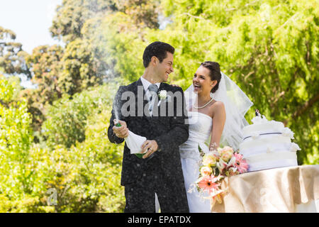 Sposa giovane con lo sposo di aprire la bottiglia di champagne al park Foto Stock