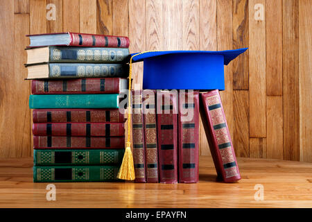 Graduazione mortarboard sulla parte superiore della pila di libri sullo sfondo di legno della parete Foto Stock