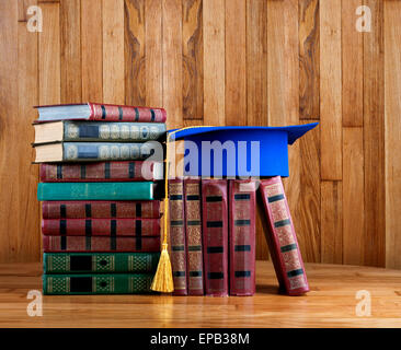 Graduazione mortarboard sulla parte superiore della pila di libri sullo sfondo di legno della parete Foto Stock