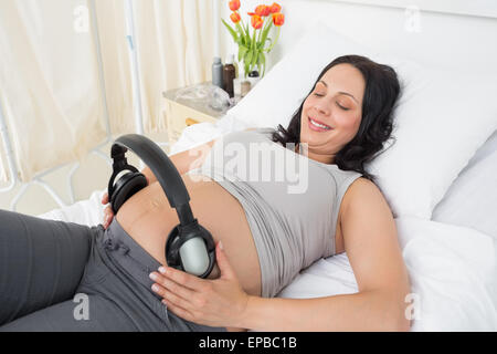 Donne incinte donna mettendo le cuffie sul suo ventre Foto Stock