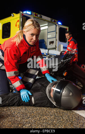 Paramedico che assiste driver in moto di notte Foto Stock