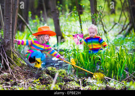 Bambini che giocano all'esterno. I bambini di età prescolare la cattura di rana con net. Un ragazzo e una ragazza la pesca nel fiume della foresta. Foto Stock