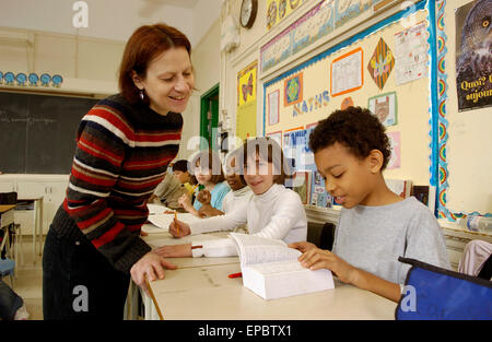 Insegnante contribuendo al grado 5 studenti che lavorano alle loro scrivanie in aula Foto Stock