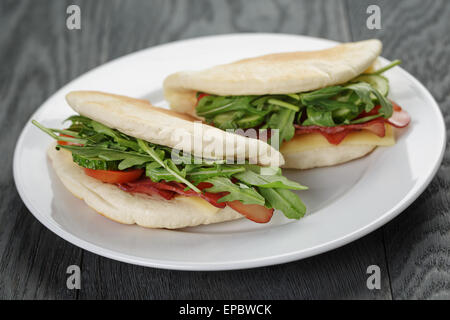 Due panini al prosciutto Rucola e Pomodori in pane pita sulla piastra, su tavola di legno Foto Stock