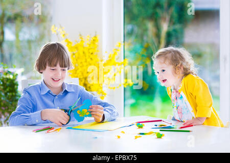 Due bambini felici, scuola ragazzo di età e poco toddler girl divertendosi insieme e verniciatura di taglio carta butterfly prima di pasqua Foto Stock