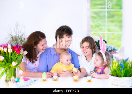 Felice famiglia giovane con tre bambini gustando la prima colazione di Pasqua in un bianco soleggiata sala da pranzo Foto Stock