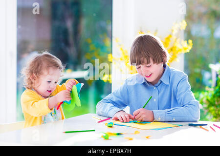 Due bambini felici, età scolastica ragazzo e ragazza toddler divertirsi insieme la pittura e il taglio della carta butterfly prima di pasqua Foto Stock