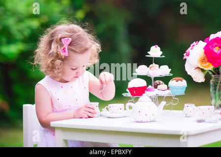 Adorabili bimbi divertenti ragazza con i capelli ricci che indossa un abito colorato per il suo compleanno giocando tea party con un orsacchiotto di peluche bambola Foto Stock