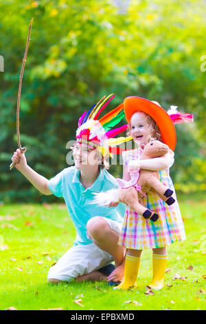 Due bambini felici, ridendo boy vestito come nativa americana con piume colorate hat e poco curly toddler girl in stivali di colore giallo Foto Stock