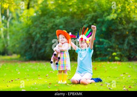 Due bambini felici, ridendo boy vestito come nativa americana con piume colorate hat e poco curly toddler girl in stivali di colore giallo Foto Stock