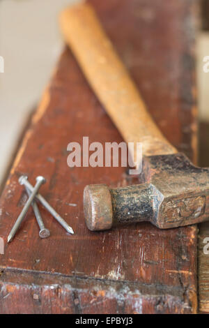 Vecchio e consumato parti martello e tre chiodi su un distressed sul banco di lavoro Foto Stock