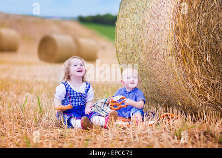 Due bambini, funny curly toddler girl e un po' di baby boy, indossando il tradizionale costume tedesco giocando in un campo Foto Stock