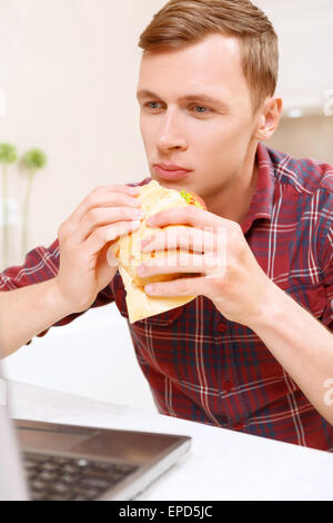 L'uomo mangiare panino nella parte anteriore del computer Foto Stock