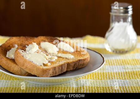 Due fette di bianco toast imburrato su una piastra con sale Foto Stock