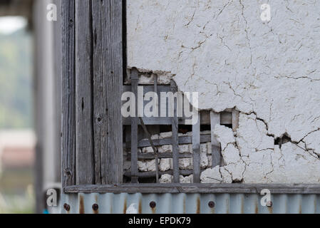 Una piscina esterna vecchio rotto e rotto la parete in gesso con il reticolo di legno dietro mostrando attraverso. Foto Stock