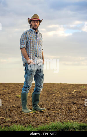 Ritratto di maschio adulto agricoltore permanente sulla fertile terra agricola del suolo, guardando alla fotocamera Foto Stock