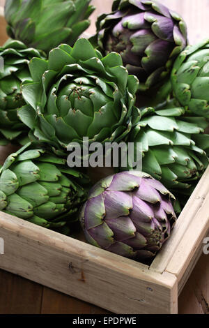 Carciofi in scatola di legno isolato su sfondo di legno Foto Stock